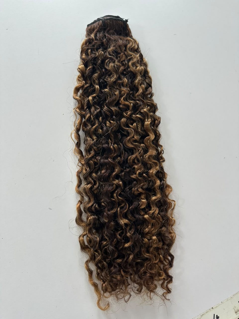 Curly hair extension weft with dark brown to light brown ombre highlights, shown against a plain white background.